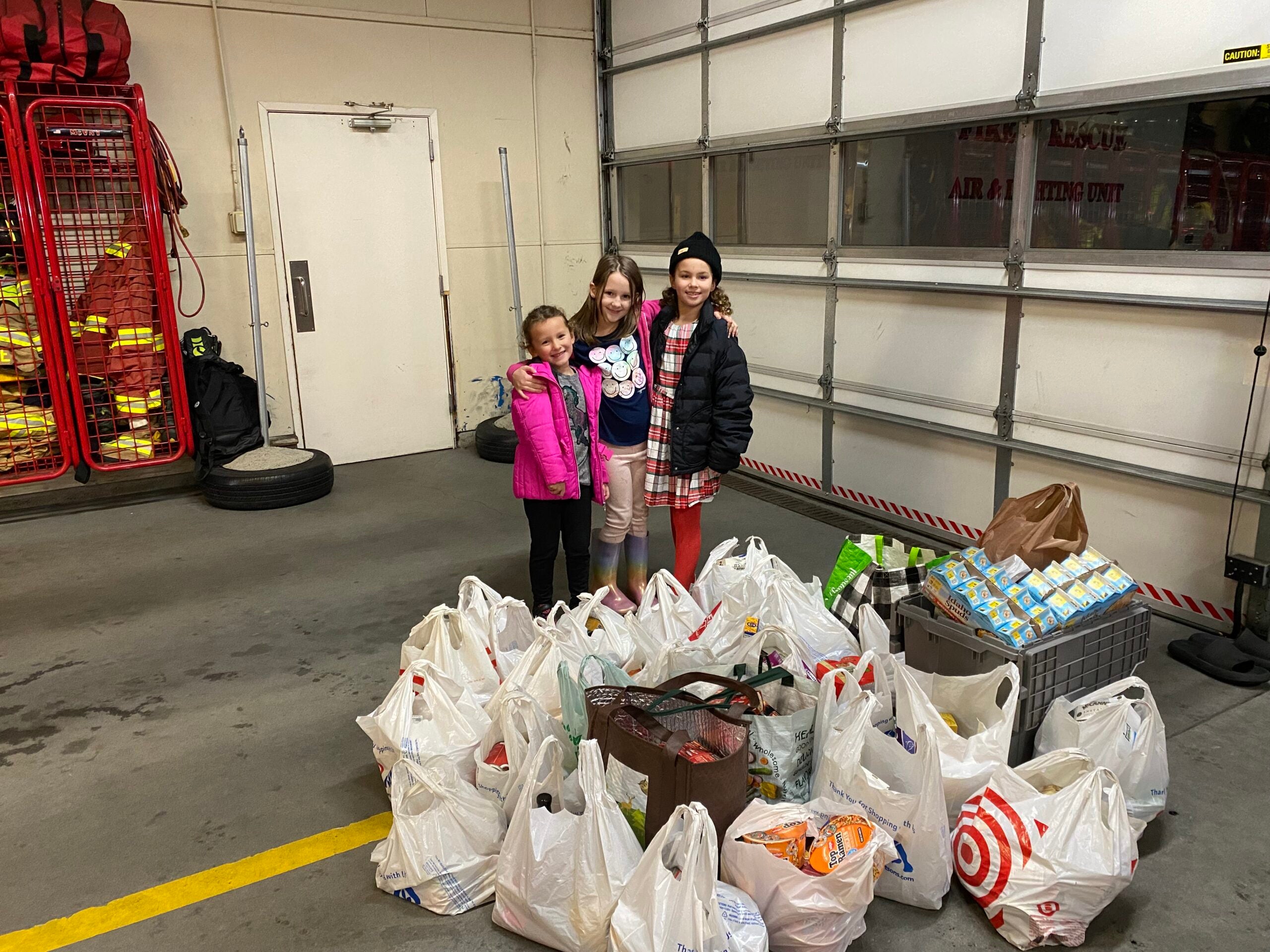 three girls standing together with bags of donations for the food drive at the santa at the station event in lakewood
